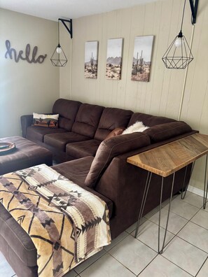 A brown leather sofa with a patterned throw blanket and a wooden side table. - The Pioneer Cottage - 1BR Near Disney & Airport (St. Cloud)