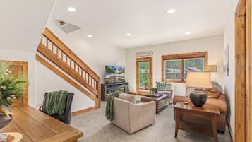 A spacious living area with a wooden staircase, a television, a sofa, and a dining table.