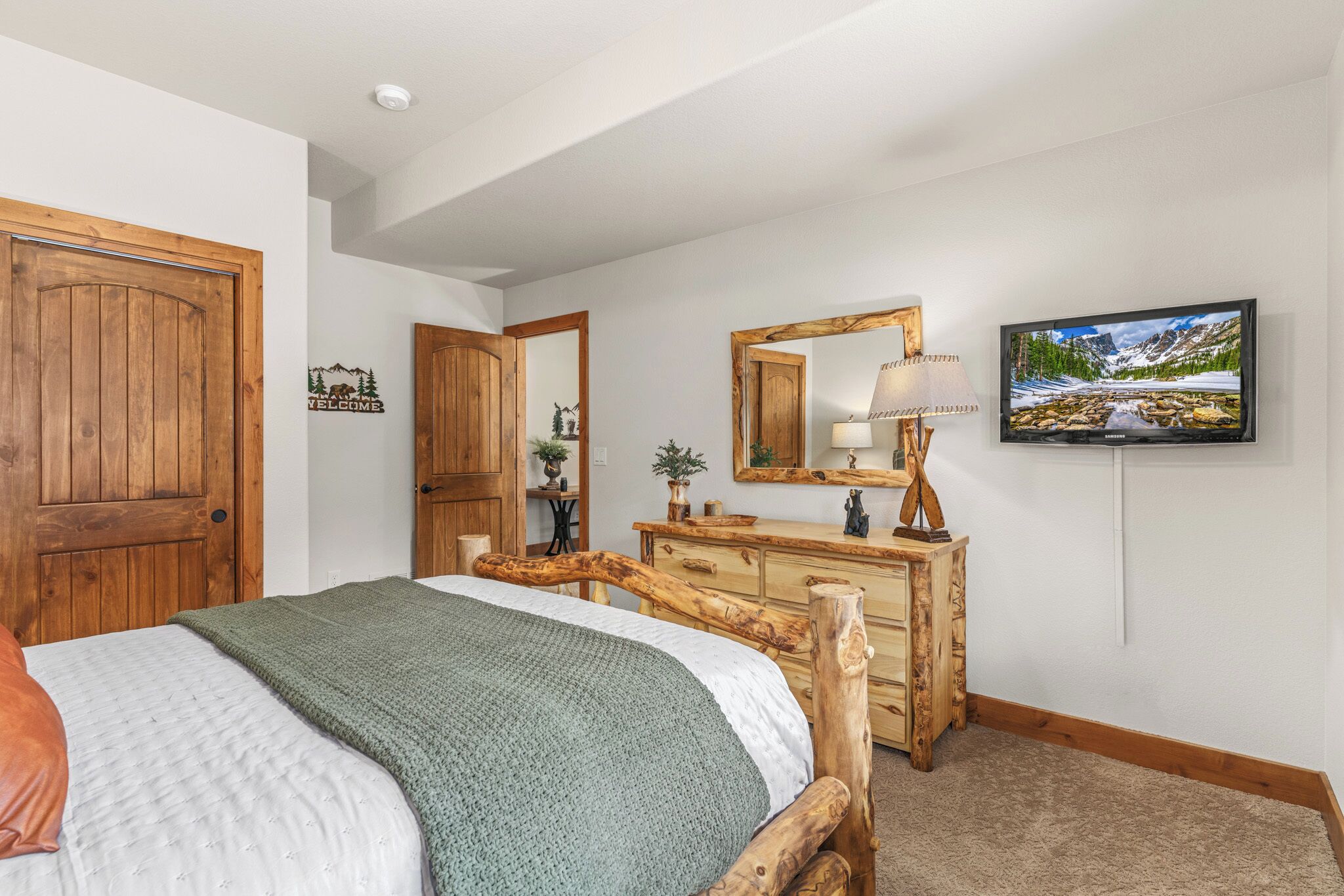 Une chambre à coucher avec un lit, une commode, un miroir, une lampe et un téléviseur.