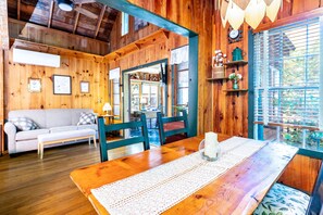 Interior acogedor de una cabaña con una mesa de madera, un sofá y una ventana con persianas.