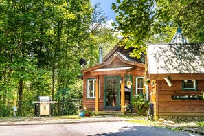 A wooden cabin with a porch, a satellite dish, and a small attached shed. - Storybook in the Smokies - Secluded, Free Pet, Hot Tub, BBQ, Washer & Dryer (Pigeon Forge)