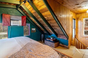 A room with a sloped ceiling, a bed, a window, and a wall-mounted heater. - Storybook in the Smokies - Secluded, Free Pet, Hot Tub, BBQ, Washer & Dryer (Pigeon Forge)