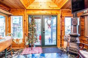 A cozy cabin interior with a wooden door, a Christmas tree, a fireplace, and a dining area. - Storybook in the Smokies - Secluded, Free Pet, Hot Tub, BBQ, Washer & Dryer (Pigeon Forge)