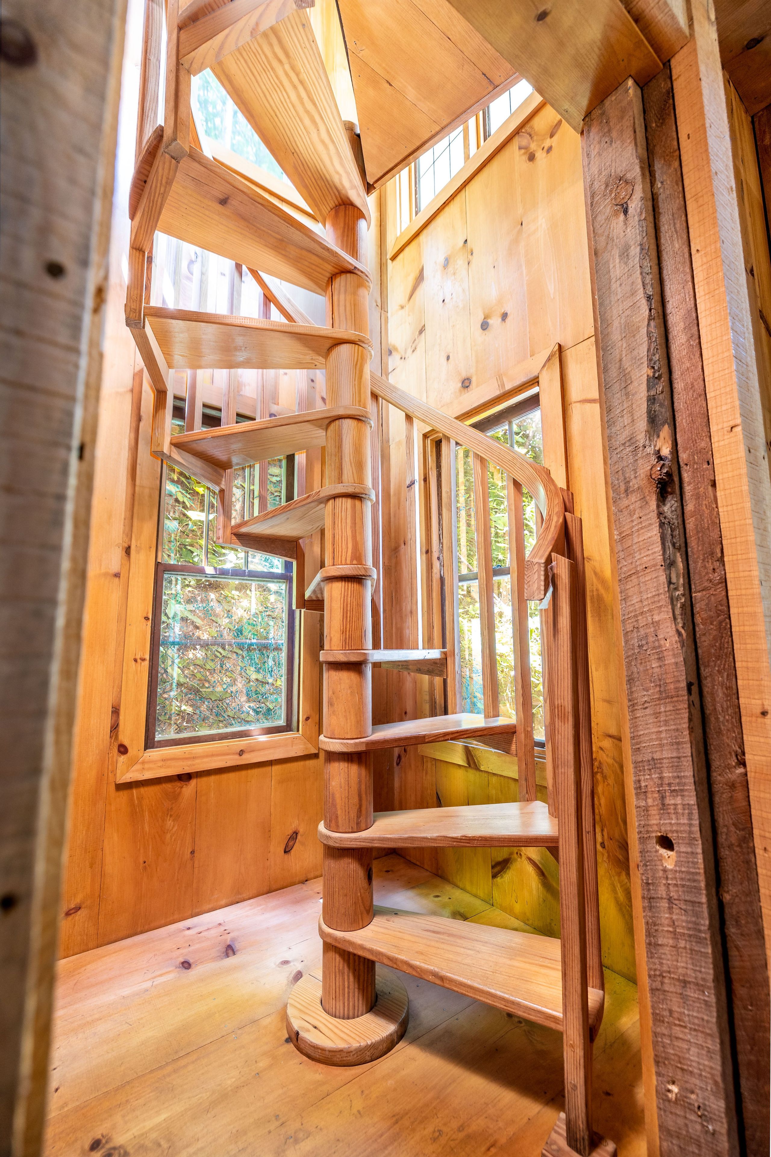 A spiral staircase inside a wooden cabin with multiple windows.
