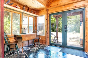 Interior de madera con comedor, una mesa, sillas, un ventanal y una puerta que da al exterior.