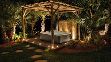Un bain à remous sous une pergola en bois, entouré de plantes tropicales.