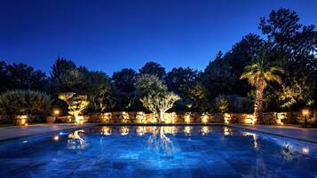 A nighttime swimming pool with stone walls and trees, illuminated by ambient lighting.