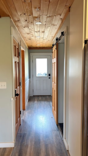 Un couloir avec un plancher en bois, une porte blanche dotée d’une fenêtre et des murs en bois.