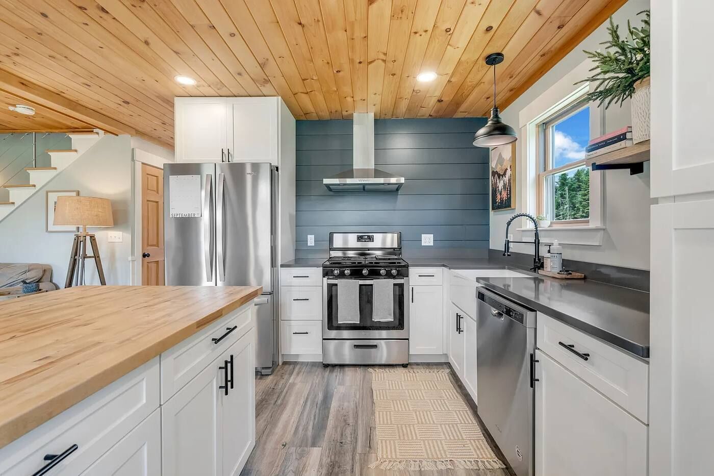 A modern kitchen with stainless steel appliances, a wooden ceiling, and a view of the outdoors.