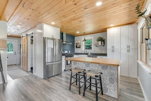 A modern kitchen with a central island, bar stools, and a stainless steel refrigerator. - Charming 3-bedroom house in serene Eustis perfect for relaxing stays! (Eustis)
