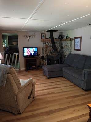Ein Wohnzimmer mit Kamin aus Stein, einem Fernseher, einem grauen Sofa und Holzboden.