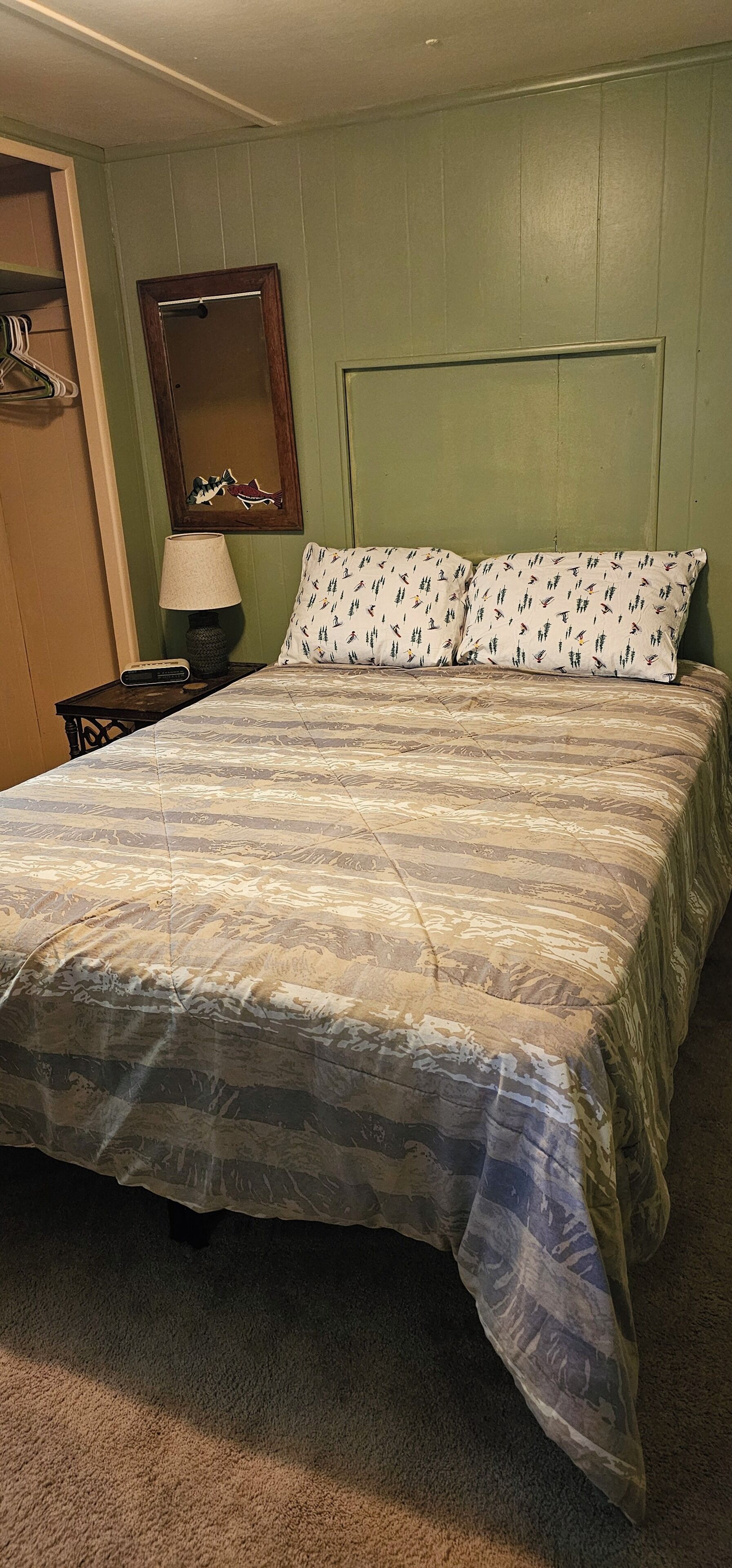 A bed with a patterned bedspread, a nightstand with a lamp, and a mirror on the wall.
