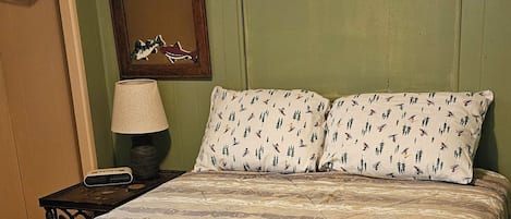 A bed with a patterned bedspread, a nightstand with a lamp, and a mirror on the wall.