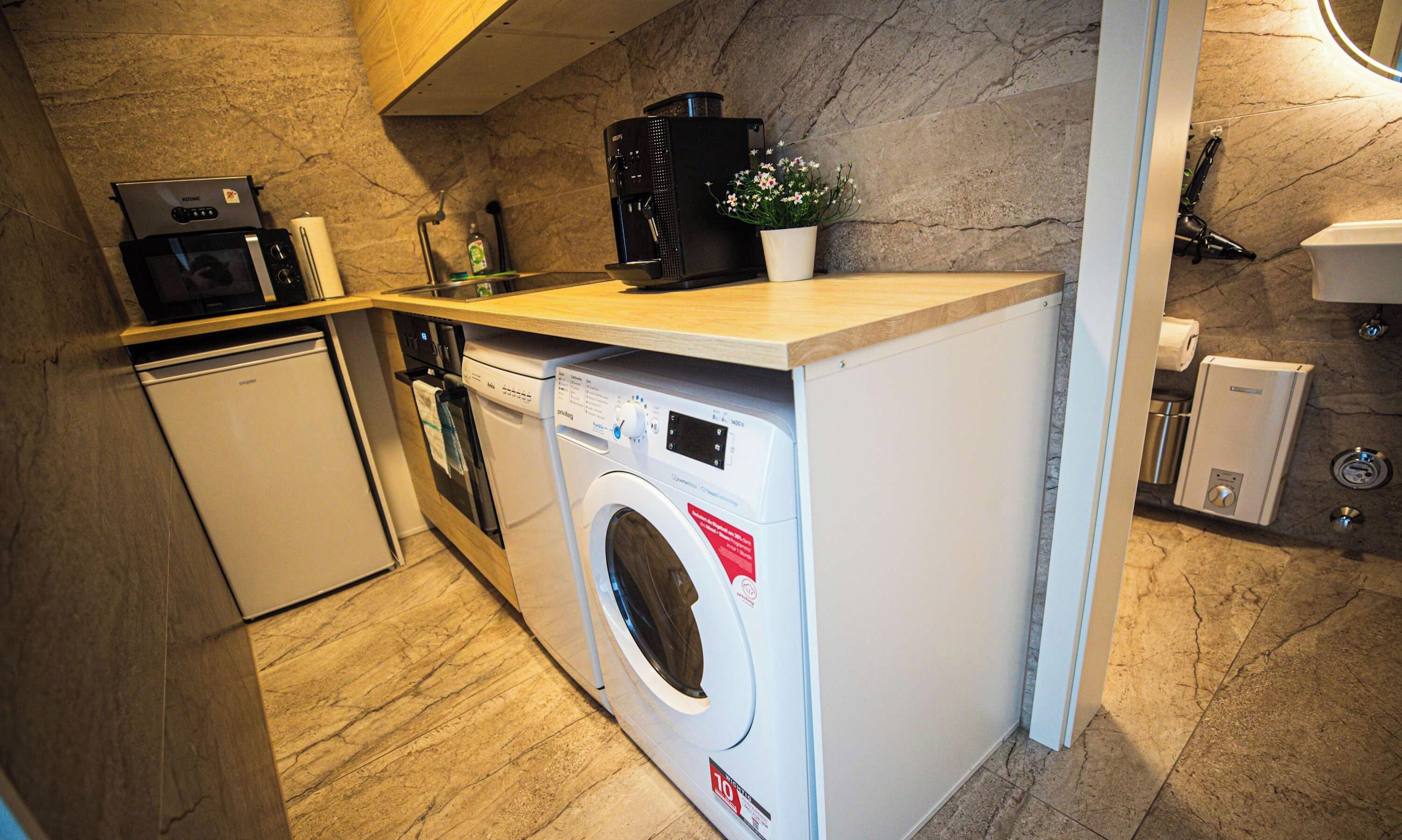 Eine kleine Küche mit Waschmaschine, Kaffeemaschine und einer Arbeitsplatte.