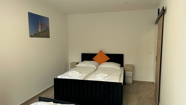 A hotel room with a double bed, two bedside tables, a nightstand, and a picture of a building on the wall. - Ferienwohnung im Bramfelder 1 (Wandsbek-Hamburg)