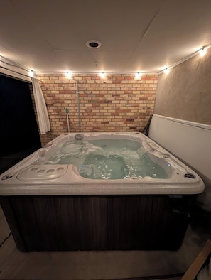 A hot tub with a brick wall backdrop, a ceiling vent, and a window with curtains. - Bountiful Haven, sleeps 10, Hot Tub, near SLC, 3 bedrooms (Bountiful)