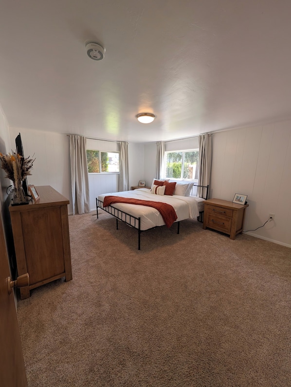 A bedroom with a bed, a bedside table, a dresser, and a window with curtains.