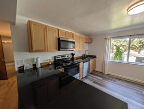 A kitchen with wooden cabinets, a black countertop, stainless steel appliances, and a window with a view.