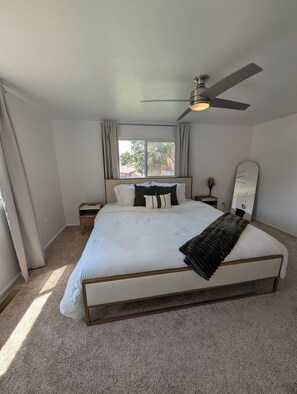 A bedroom with a large bed, a ceiling fan, a window with curtains, a bedside table, and a mirror. - Bountiful Haven, sleeps 10, Hot Tub, near SLC, 3 bedrooms (Bountiful)
