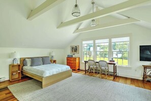 Quarto com uma cama grande, uma escrivaninha e uma cadeira, com janelas que proporcionam luz natural.