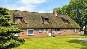 Ein traditionelles Backsteinhaus mit einem Reetdach, einer Haustür und einer kleinen Veranda.