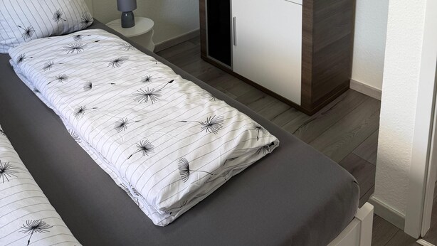 Ein Schlafzimmer mit einem Bett, einem Kleiderschrank, einem Nachttisch mit Lampe und einer Wand mit gerahmten Bildern.