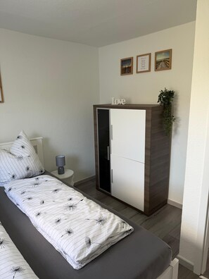 A bedroom with a bed, a wardrobe, a bedside table with a lamp, and a wall with framed pictures. - "Reethus – A Little Getaway" Vacation Rental in a Quiet Setting, Near the North Sea and the Islands (Bosbüll)