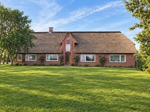 A two-story brick house with a gabled roof, a front porch, and a well-maintained lawn. - "Reethus – A Little Getaway" Vacation Rental in a Quiet Setting, Near the North Sea and the Islands (Bosbüll)
