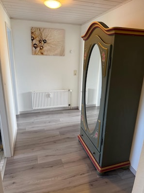 Un couloir avec un radiateur, un plancher en bois et un grand miroir fixé à un meuble.