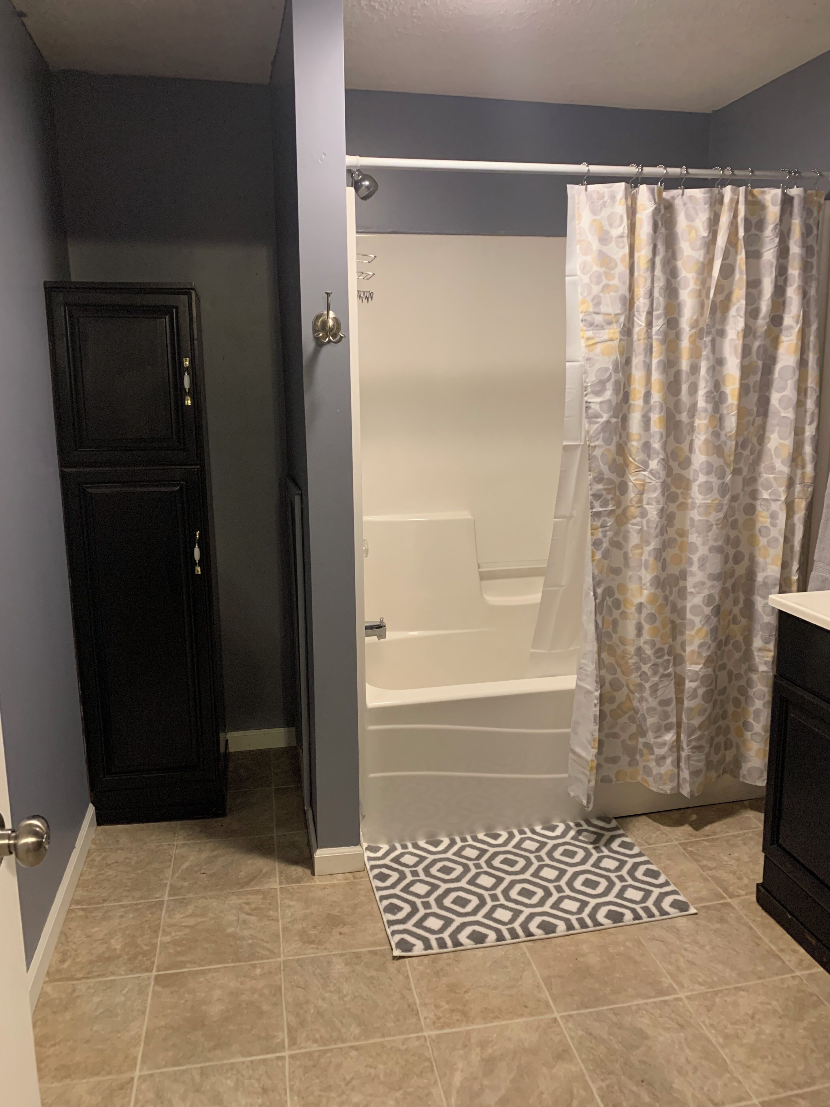 A bathroom with a shower, a patterned rug, and a door.