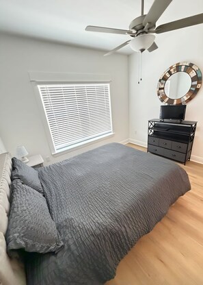 Une chambre à coucher avec un lit, un ventilateur de plafond, une commode et une fenêtre avec des stores.