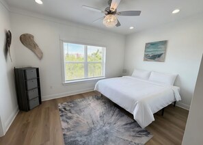 Ein Schlafzimmer mit einem Bett, einem Deckenventilator, einem Fenster mit Jalousien, einem Gemälde an der Wand und einem schwarzen Stauraum.