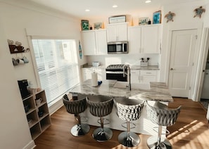 A modern kitchen with white cabinets, a central island with bar stools, and a microwave above the stove. - SEACHELES Orange Beach BIG FALL Savings.  3 brd 5 beds 4 Baths SLEEPS 10 (Orange Beach)