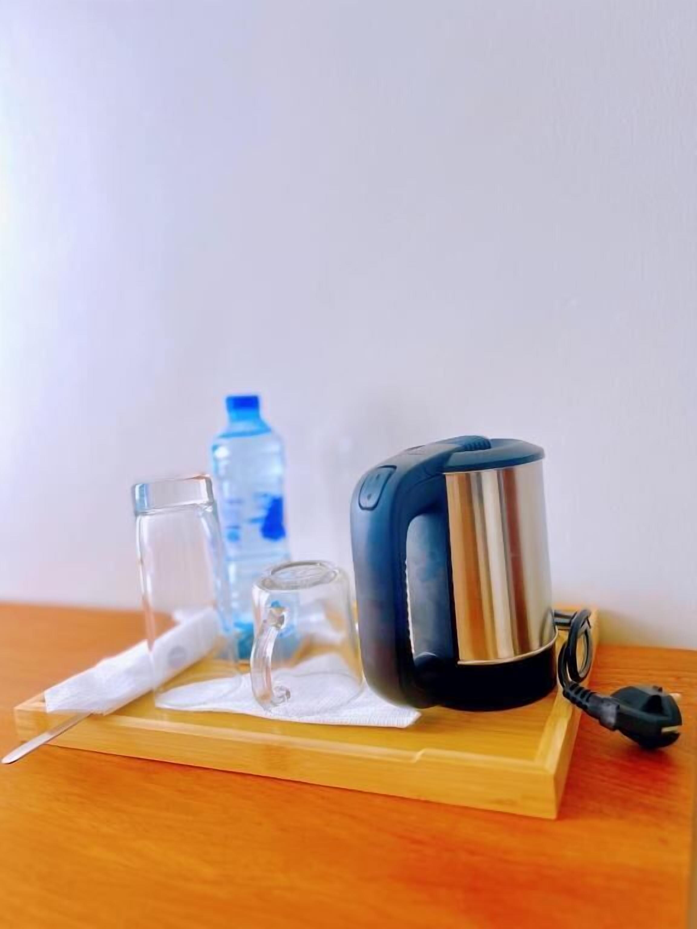 A kettle on a wooden tray with a glass and a bottle of water.