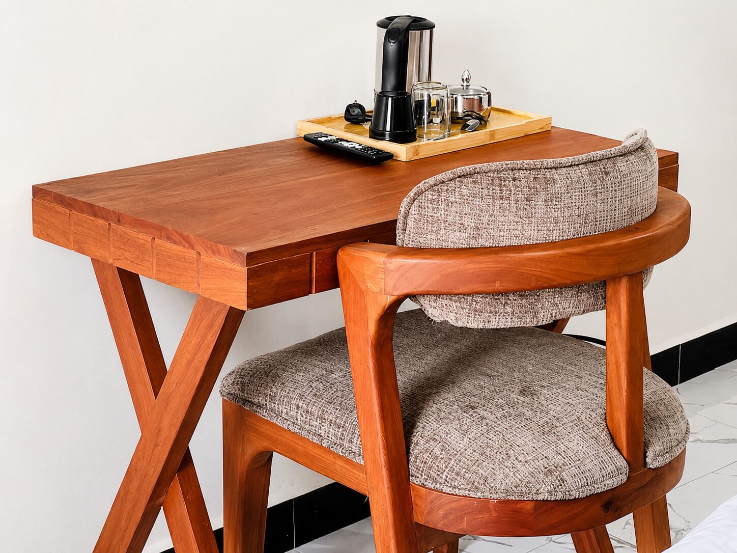 Een houten bureau met een koffiezetapparaat, een afstandsbediening en een glazen vaas op een dienblad.
