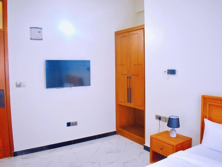 Habitación de hotel con cama, mesita de noche con lámpara, armario, televisor montado en la pared y una puerta.