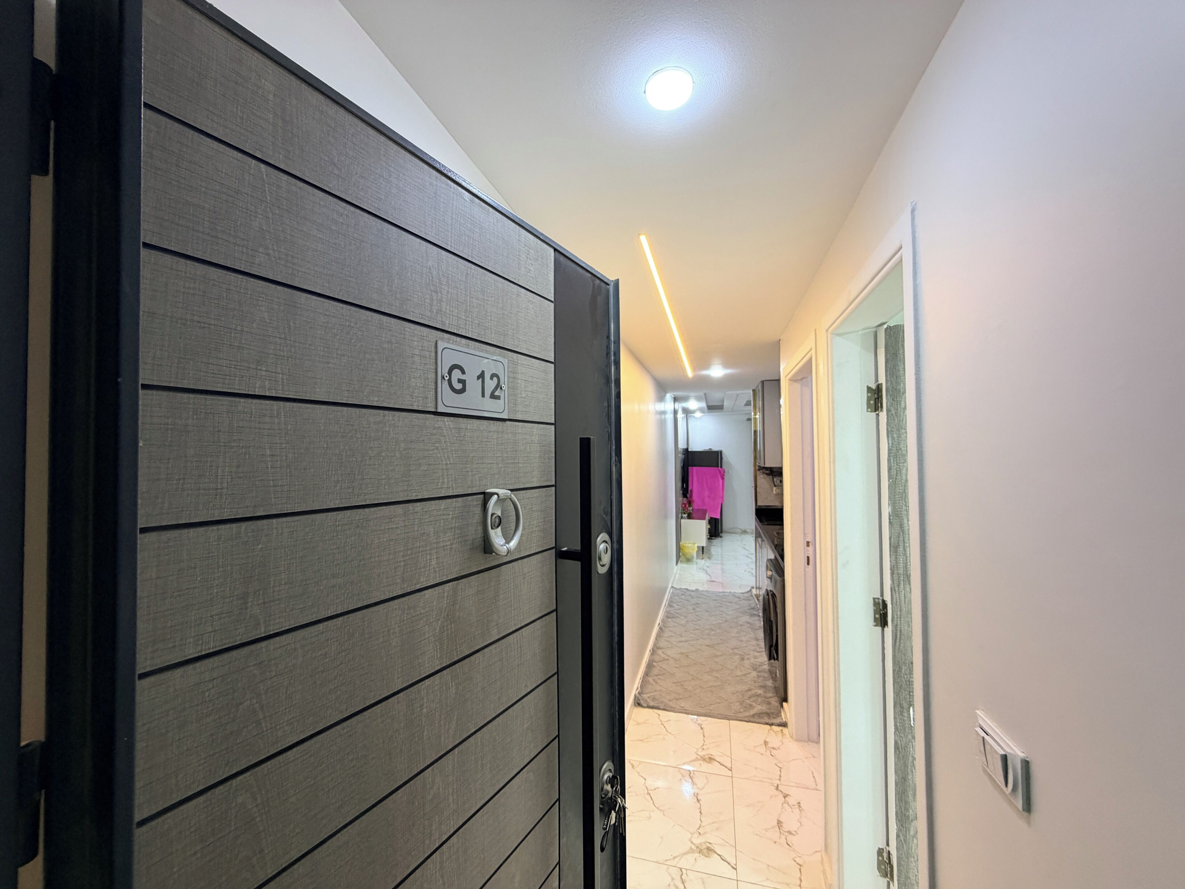 A hallway with a door labeled 'G 12' leading to a room with a tiled floor.