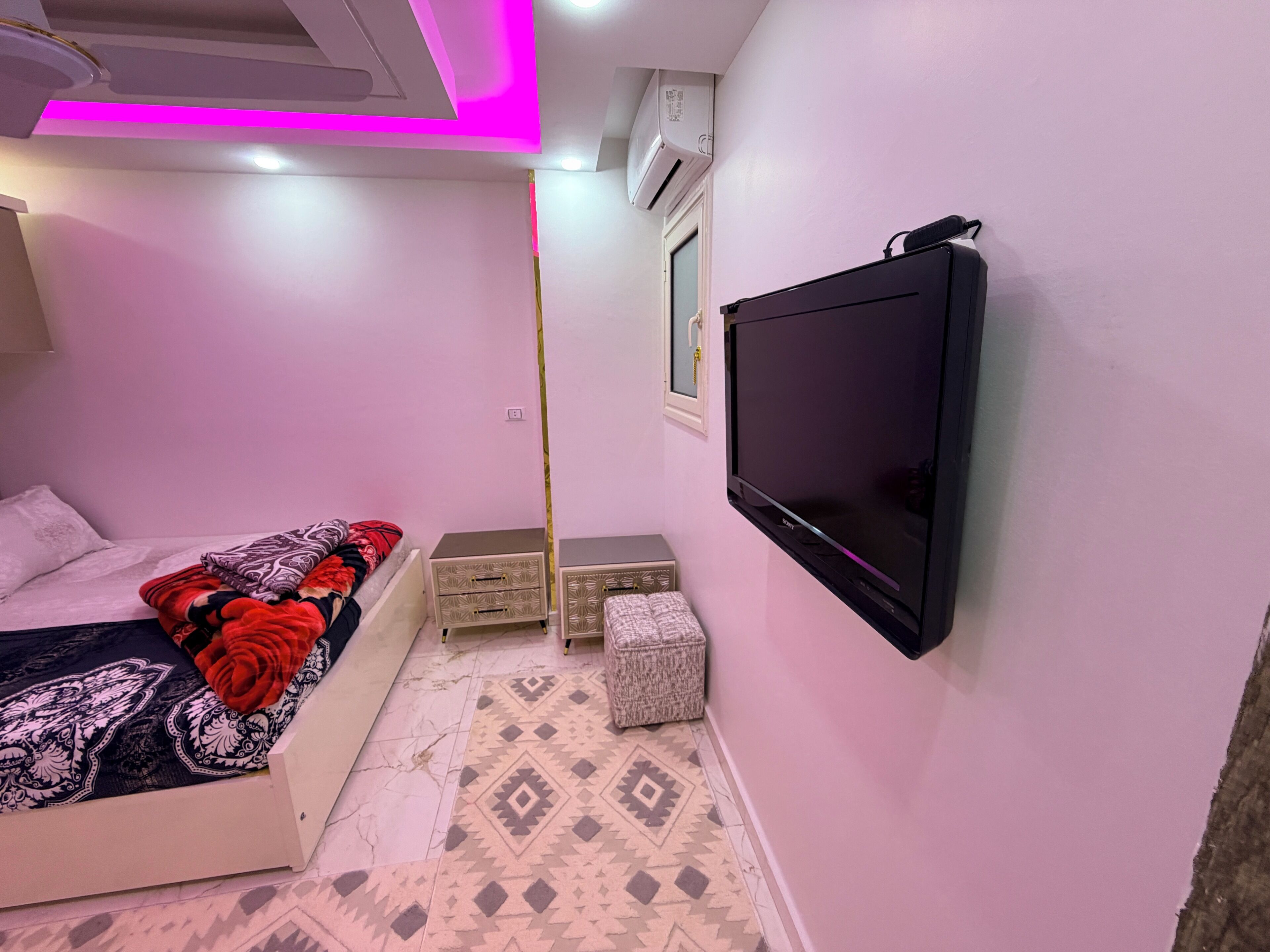 Ein Schlafzimmer mit einem Bett, einem Fernseher, einem Kleiderschrank und einem gemusterten Boden.