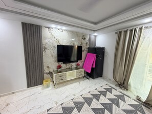 Ein Wohnzimmer mit Flachbildfernseher, schwarzem Kühlschrank, Teppich mit Muster und Marmorboden.