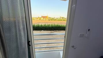 A room with a sliding glass door leading to a balcony with a metal railing, a power outlet, and a wall-mounted light switch.