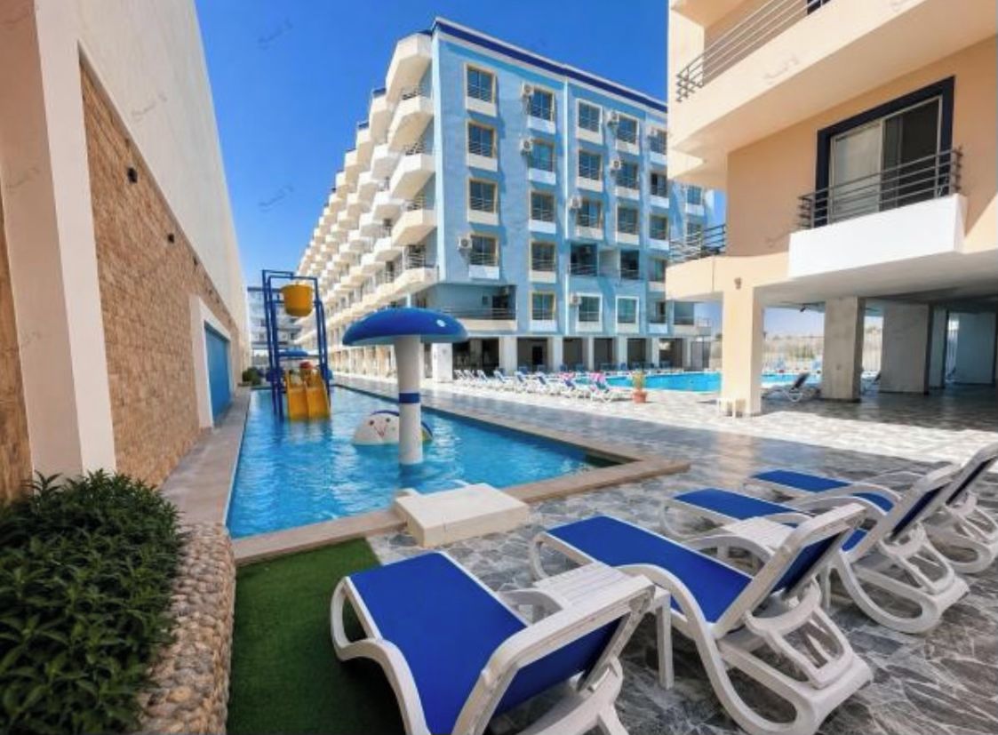 Ein Hotelpoolbereich mit Liegestühlen, einem Pool und einem Gebäude mit mehreren Balkonen.