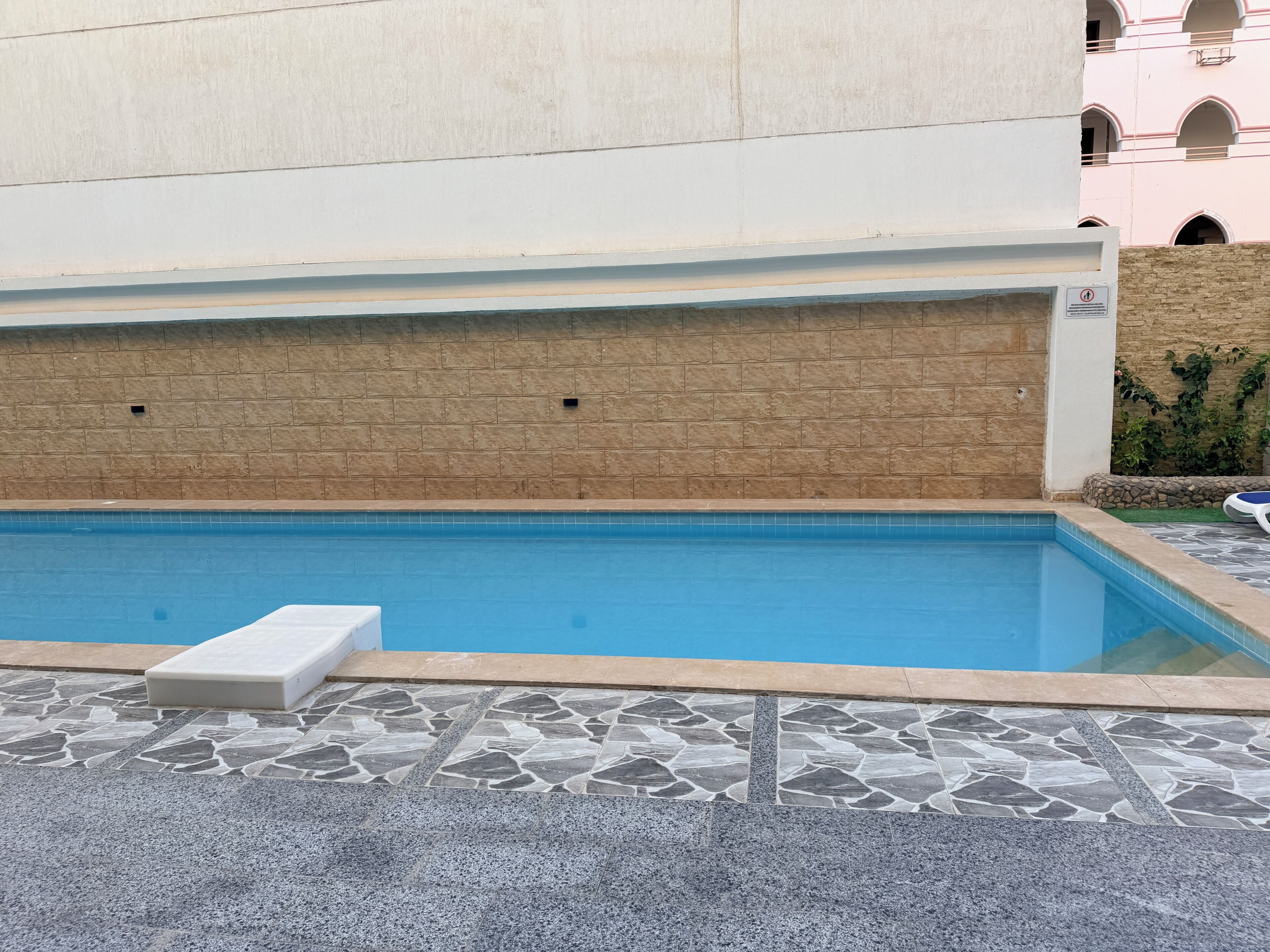 Una piscina con deck de piedra y una silla de descanso blanca.