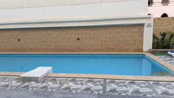 Una piscina con deck de piedra y una silla de descanso blanca.