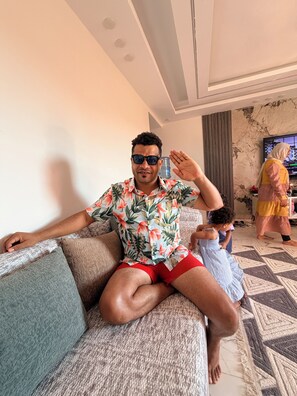 A person sitting on a sofa in a room with a television, a water dispenser, and a patterned rug. - Lavonda Beach resort hurghada ALAHYA (Hurghada)