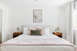 A bedroom with a bed, two bedside tables, a nightstand, a wall-mounted painting, and a window with curtains. - Hummingbird Hideaway - Executive Resort-style Condo (Phoenix)