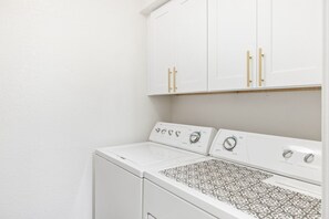 A laundry area with a front-loading washer and dryer, white cabinets above, and a patterned floor. - Hummingbird Hideaway - Executive Resort-style Condo (Phoenix)