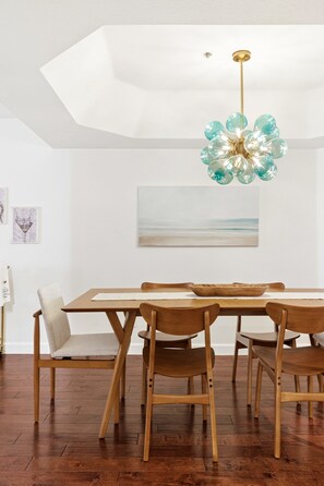 A dining area with a wooden table and chairs, a modern chandelier, and a painting on the wall. - Hummingbird Hideaway - Executive Resort-style Condo (Phoenix)