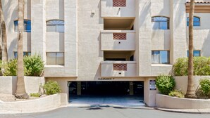A multi-story building with a parking garage entrance, palm trees, and a sign indicating 'CLEARANCE 7' for parking. - Hummingbird Hideaway - Executive Resort-style Condo (Phoenix)