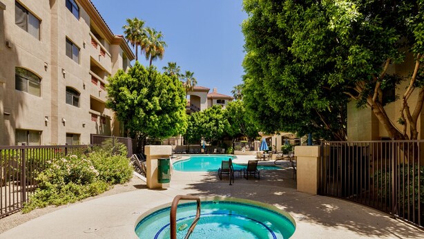 A swimming pool with lounge chairs and a hot tub, surrounded by trees and a building with balconies. - Hummingbird Hideaway - Executive Resort-style Condo (Phoenix)