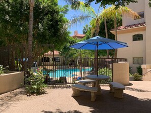 A pool area with a fence, a table with benches, and a blue umbrella. - Hummingbird Hideaway - Executive Resort-style Condo (Phoenix)